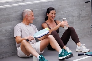 Two adults resting after playing pickleball, drinking water and talking during a break